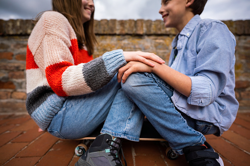 Teenage girl and boy sitting on skateboard in park