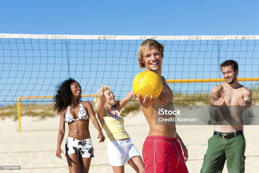 Friends playing beach volleyball Group of friends - women and men - playing beach volleyball, one in front having the ball Beach Stock Photo