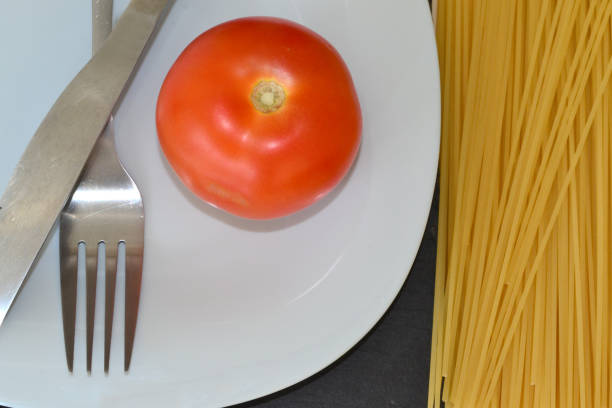 there is a tomato, utensils and pasta nearby on a blue plate