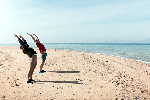 Beautiful couple doing sun salutation on the beach