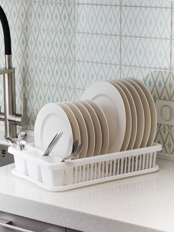 A plastic dish drying rack stands at the sink in the kitchen with clean dishes inside. Organization of space in the kitchen, kitchen utensils.