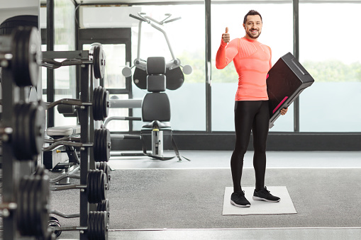 Man with a step aerobic platform showing thumb up at the gym