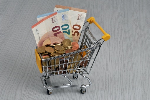 Purchasing power concept with a supermarket trolley full of euros close up on a gray background