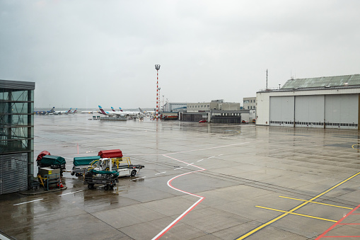 Wide shot of planes parked up at an airport ready to take passengers on vacation. The weather is rainy.