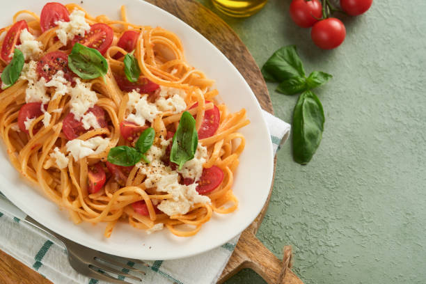 salat-caprese oder pasta-spaghetti gebrochen mit basilikum und mozzarella ala caprese auf weißem teller auf grünem rustikalem holzhintergrund. traditionelle italienische küche. italienisches food-konzept. draufsicht. rezept. - caprese salad antipasto wine mozzarella stock-fotos und bilder