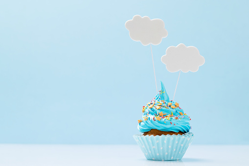 Blue cream cupcake with speech bubble decor on yellow background with copy space