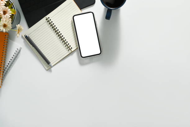 istock Smartphone with empty screen, notebook, coffee cup and laptop on white table. Top view, blank screen for advertise text. 1532919777