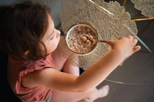 Child girl eating with spoon from the bowl at home. stock photo