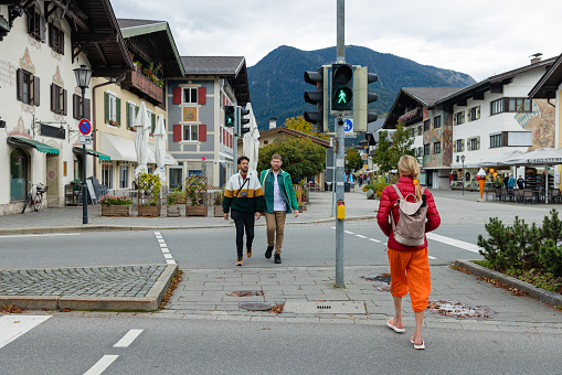 A wide angle front view of a same sex couple crossing the road in Garmisch town centre. They are crossing safely using contactless technology at the crossing with hygienic contact free waving to activate the crossing.