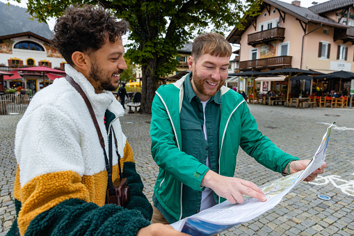 A close up view of a same sex couple who are map reading and working together and navigating their way around Garmisch town in south Germany. They are stood in the town square and working out the direction for the walking trails nearby,