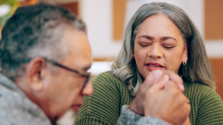 Senior couple praying in home for faith, spiritual peace and worship of trust in God. Man, woman and eyes closed for prayer, christian religion and retirement of respect, jesus christ and holy praise