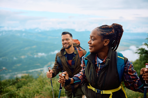 Couple of hikers walking on a hill while using hiking poles. Focus is on African American woman. Copy space.