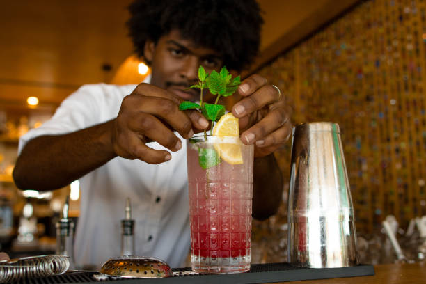 latin bartender with curly hair putting a top of mint in the cocktail stock photo