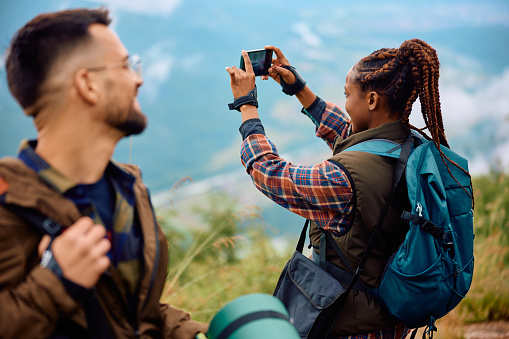 African American woman photographing nature with cell phone while hiking with her friend.