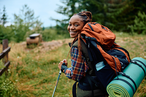 Happy African American female hiker enjoying in nature and looking at camera.