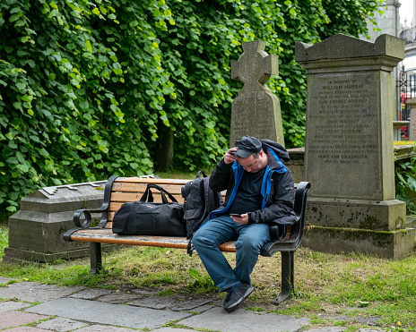 27 June 2023.Aberdeen,Scotland. This is a man with a holdall and rucksack, seated on a bench and browsing on his mobile phone.