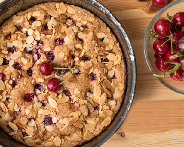 Delicious homemade cherry pie or cherry cake with sour cherries and almonds. Served warm in a round baking pan isolated on wooden table background from above.