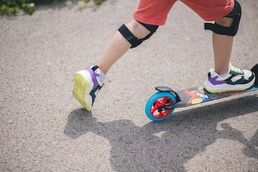 Child riding on scooter on asphalt road in summer. Concept of freedom and mobility.