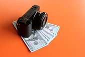 Mirrorless camera and money on orange background with copy space.
