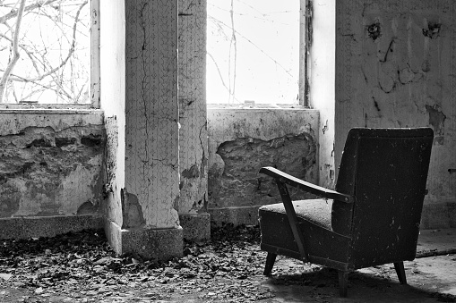 A grayscale of chair in a dilapidated room surrounded by bare brick walls