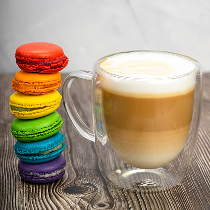 Multicolored macaroons and a transparent mug of cappuccino. The concept of freedom and love. Romance and sweets. Food photo.