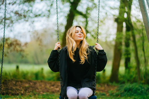 Joyful and youthful woman on a swing at the park. Concept pf people and no limit age to play and have fun. Female in outdoors leisure activity using swing and enjoy life