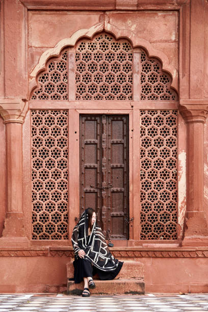 east asian woman in black dress sitting on steps of entrance to indian temple - taj mahal mahal door temple imagens e fotografias de stock