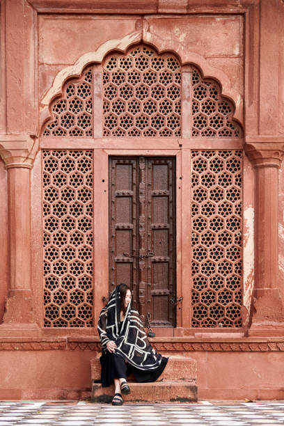 восточноазиатская женщина в черном платье сидит на ступеньках входа в индийский храм - taj mahal mahal door temple стоковые фото и изображения