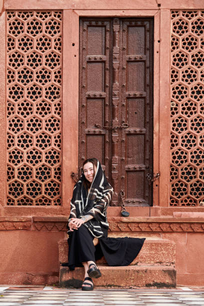 donna dell'asia orientale in vestito nero che si siede sui gradini dell'ingresso al tempio indiano - taj mahal mahal door temple foto e immagini stock