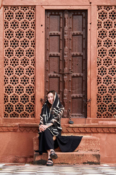 east asian woman in black dress sitting on steps of entrance to indian temple - taj mahal mahal door temple imagens e fotografias de stock