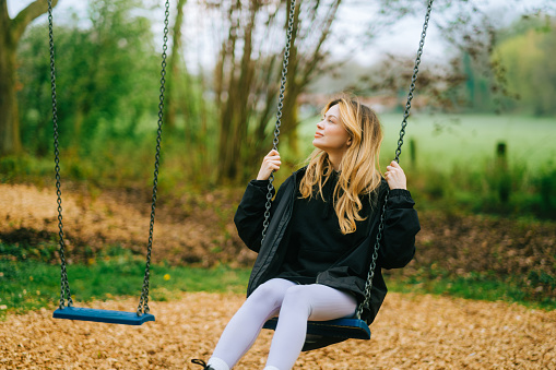 Joyful and youthful woman on a swing at the park. Concept pf people and no limit age to play and have fun. Female in outdoors leisure activity using swing and enjoy life