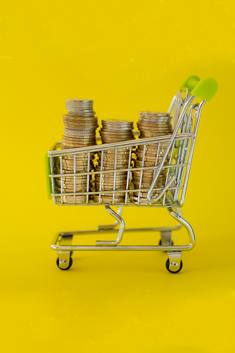 Many coin in mini shopping cart on yellow background