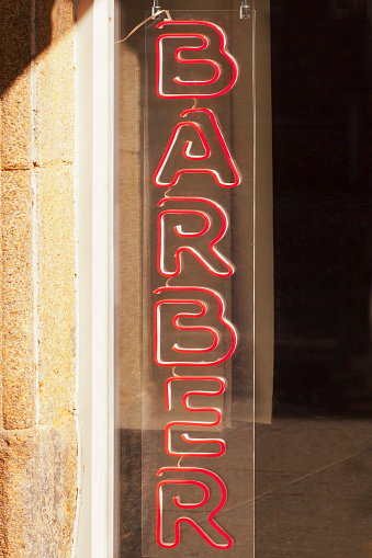 Barbershop old fashioned sign in the sunlight, red neon light.  A Coruña, Galicia, Spain.