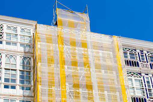 Scaffolding and netting in a restoring construction site. A Coruña city traditional  galerías, old glass facades. Low angle view from city street, Galicia, Spain.