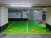 Underground parking spaces reserved for electric vehicles only. Small wall mounted charging plugs, green painted cement floor, no people