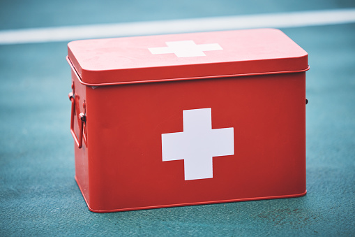 First aid, kit and health equipment for medical emergency, response and treatment kit isolated in a blurred background. Red, cross and medicine on a sports ground or court for fast health or cure