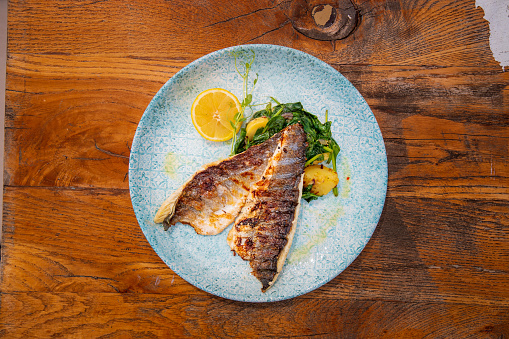 Directly above grilled fish fillets served with boiled chard and potatoes in a plate on wooden restaurant table, fine dining healthy eating