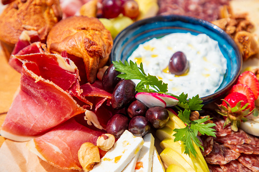 Close-up on delicious assortment of cheese and smoked meat delicatessen served on wax paper with corn bread and sliced fruit, olives and nuts, dipping cream in a bowl in the middle, fine dining appetizer