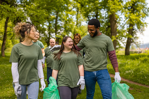 Group of environmentalist including people with down syndrome volunteers walking in a forest with cleanup gear