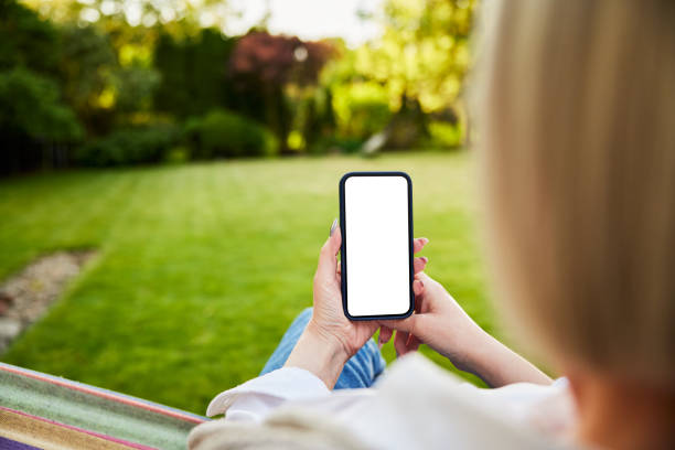 Close up of woman using phone in garden sitting in hammock with blank mock up screen stock photo