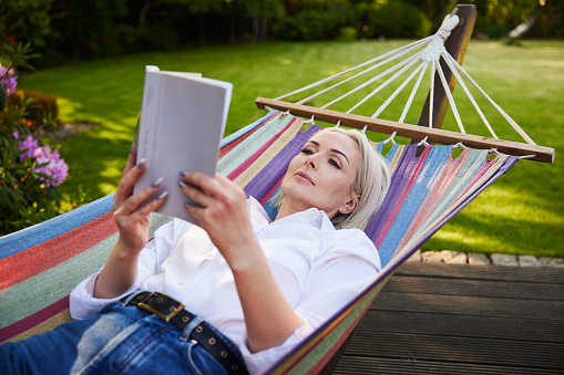 mature woman in white sitting on deck chair in the garden at the lake in front of her house