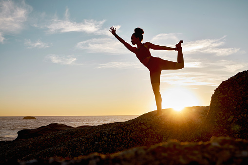 Fitness, woman and yoga stretching on the beach during sunset for spiritual wellness, training or workout. Active female in calm, zen or warm up stretch for healthy exercise posing on a ocean rock