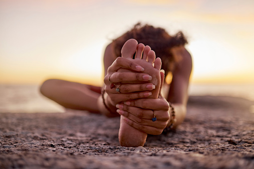Stretching, peace and feet of a woman on beach for yoga, training and exercise during sunset. Fitness, sand and legs of girl doing warm up before workout or pilates for wellness and relax by the sea