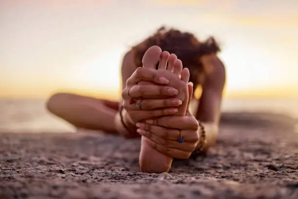 Photo of Stretching, peace and feet of a woman on beach for yoga, training and exercise during sunset. Fitness, sand and legs of girl doing warm up before workout or pilates for wellness and relax by the sea