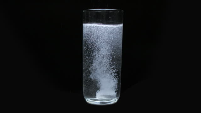 Aspirin falling into a glass of water on black background, slow motion