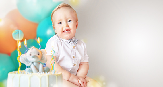Banner of happy cute little boy (1 year old) with delicious, tasty birthday cake (sweets with candles of number one and decoration).  Celebrating child's first year birthday. Copy space. Empty space for your message.