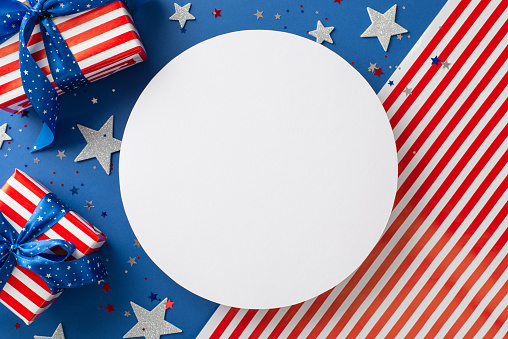 USA-themed festive greetings. Overhead shot reveals artistry of shiny stars, glistening confetti, gift boxes wrapped thematically— presented on flag backdrop with empty circle, perfect for text or ad