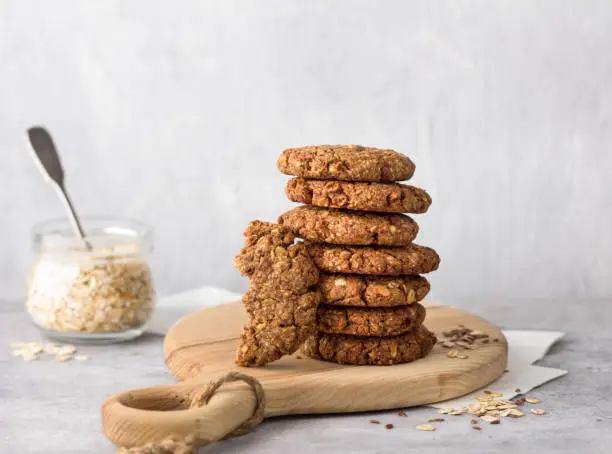 Healthy oatmeal cookies with dates, nuts and flaxseed on a wooden board on a gray textured background. Delicious homemade vegan food
