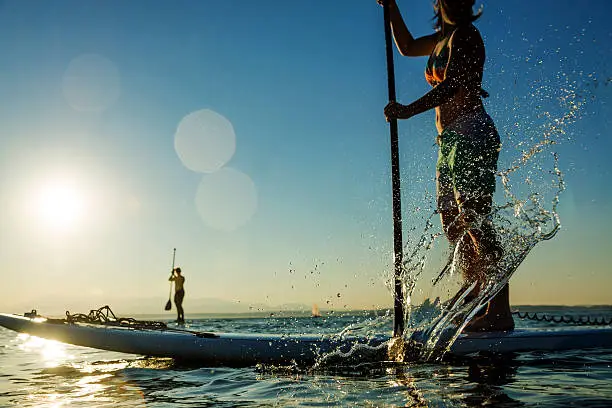 Woman paddling stand up paddle board splashing water.