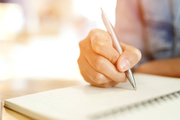 istock close up hand young man are sitting using pen writing Record Lecture note pad into the book on the table wood. 1533607847